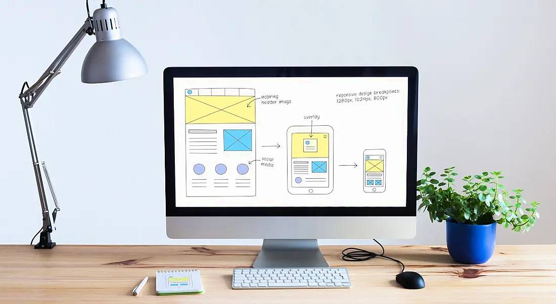 A large computer screen on a wooden desk, showing design iterations. This symbolises UX design skills.