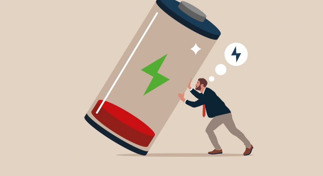 A cartoon image of a man pushing a giant battery upright. The battery itself is in the red, symbolising burnout at work.