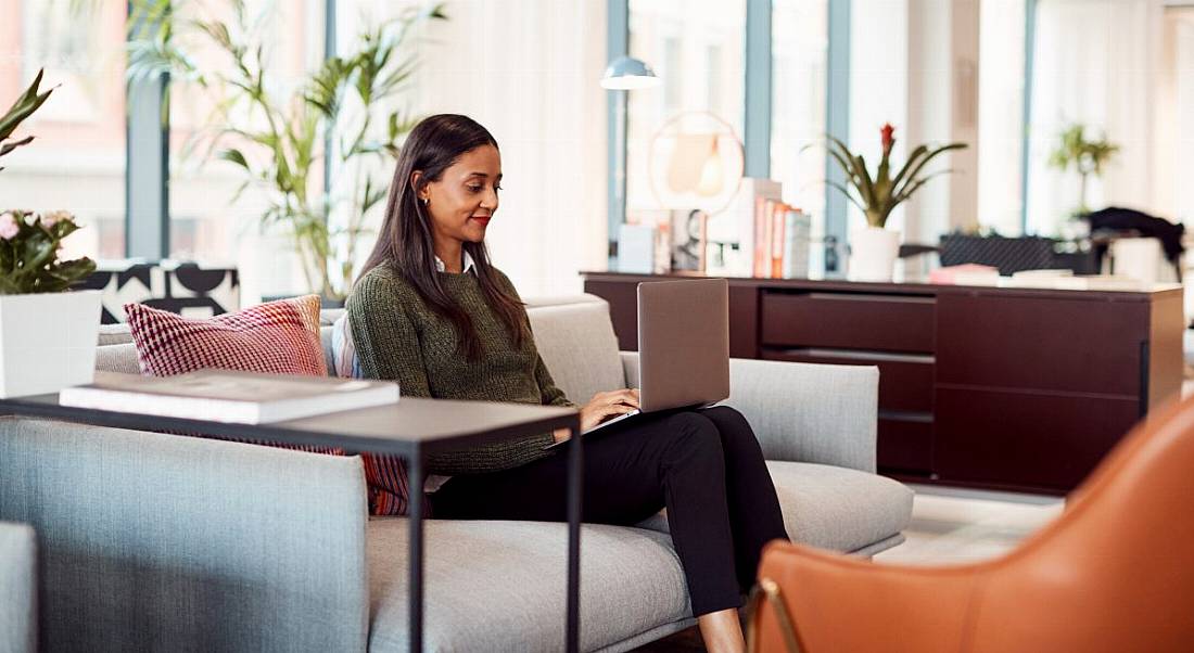 A young woman sitting on a couch working on a laptop, symbolising flexible working.