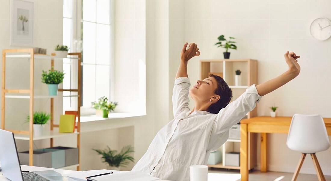 A woman working from home, stretching her arms, symbolising taking a break in a hybrid workplace.