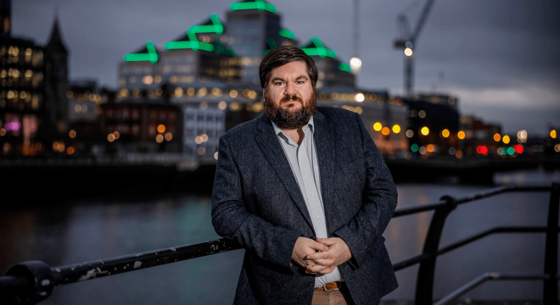 Dr Joe Fitzsimons, founder of Horizon Quantum Computing, leans against a railing with the nighttime Dublin cityscape behind him.