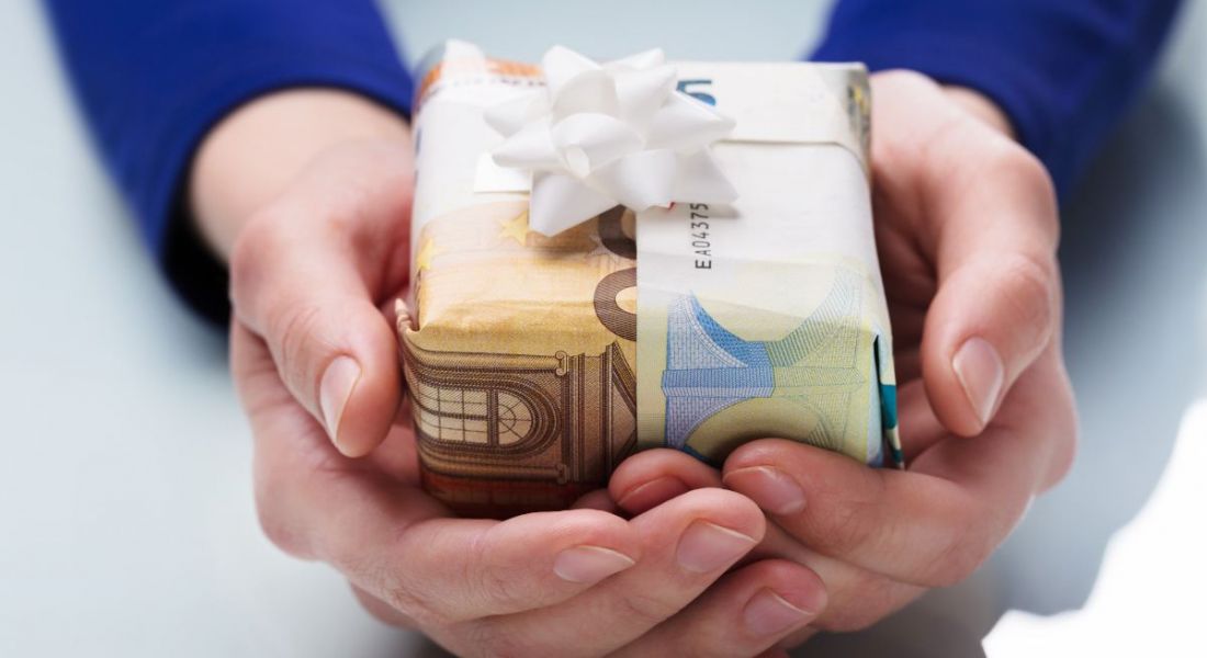 A pair of hands holding a gift parcel that is wrapped using euro notes and has a ribbon on top.
