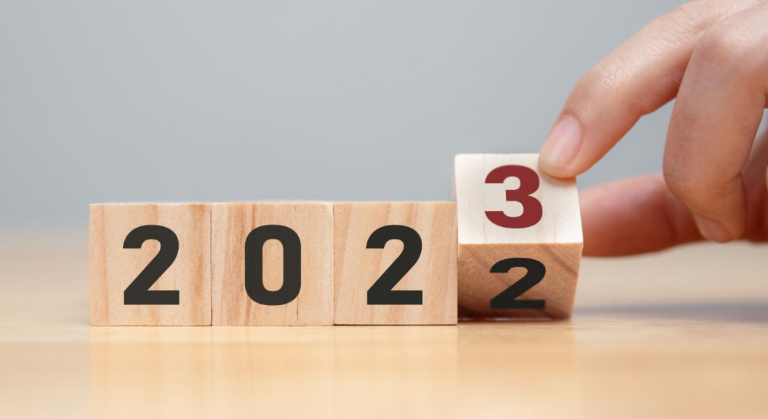 Person's hand turning a wooden block with a two on it into the side with a three representing a change to the calendar from 2022 to 2023.