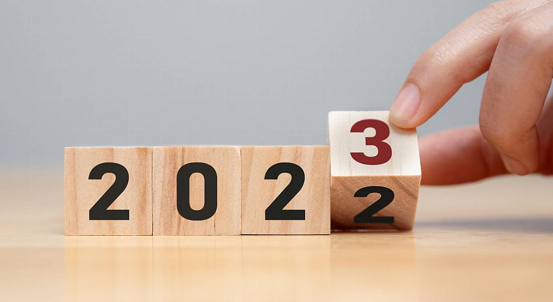 Person's hand turning a wooden block with a two on it into the side with a three representing a change to the calendar from 2022 to 2023.