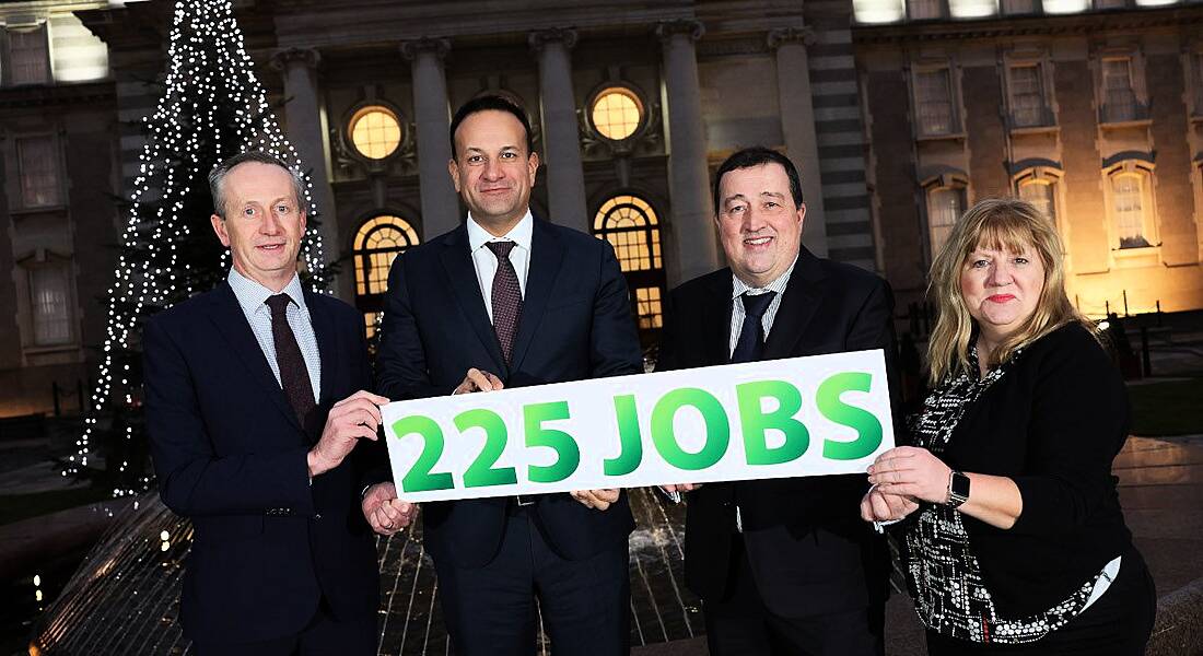 Four people standing outside in front of a lit up Christmas tree, holding a sign that says '225 jobs'.