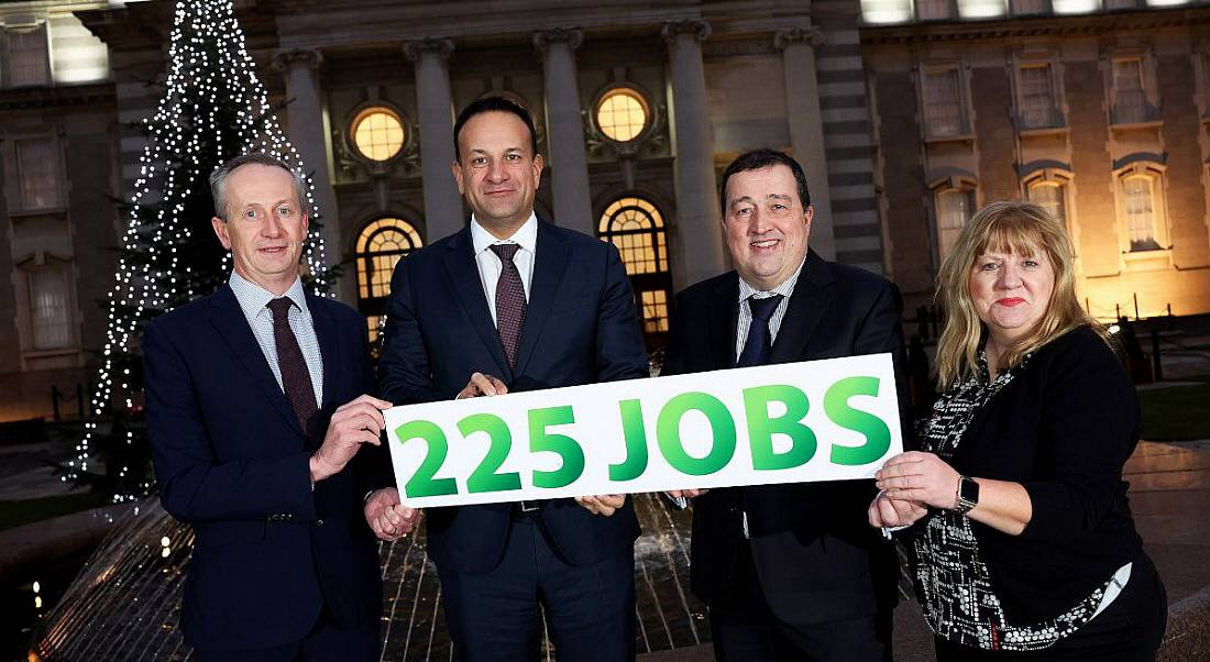 Four people standing outside in front of a lit up Christmas tree, holding a sign that says '225 jobs'.