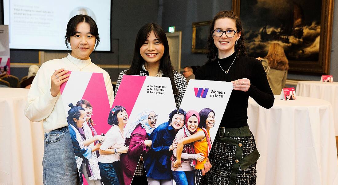 Three young women stand holding a large W at a Huawei event.