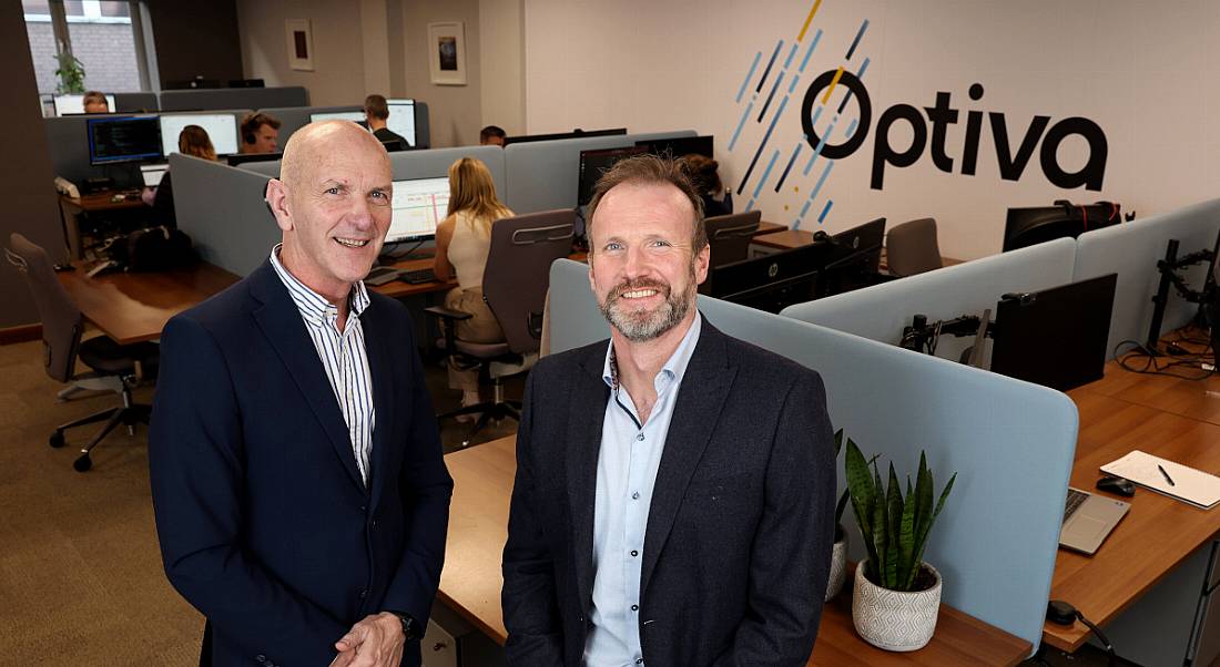 Two men stand in an office with the Optiva logo on the wall behind them.