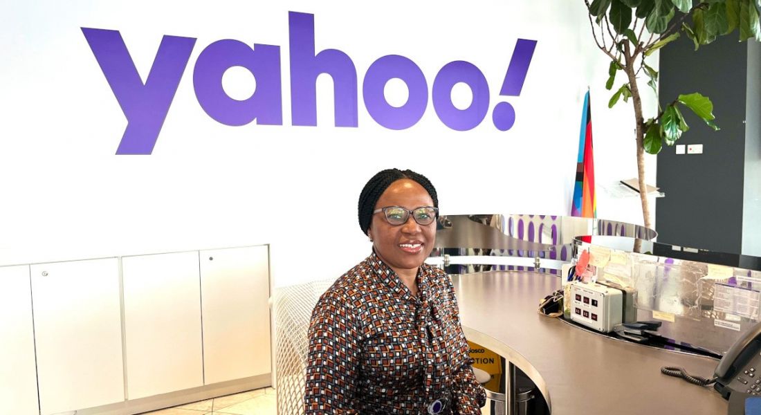 A woman sitting at a desk with the Yahoo logo in the background on a wall. She is Ndidi Opute, a third-party security risk analyst.