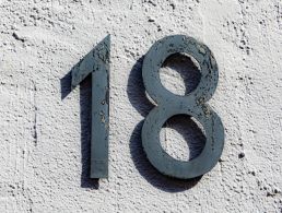 A sign with the number 18 on a brown brick wall next to the front door of a house.