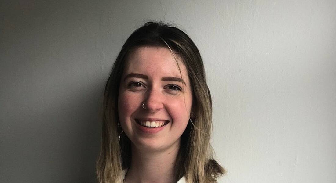 A woman smiles in front of a light coloured wall. She is Jess Wyer, a cyber risk analyst at Deloitte.