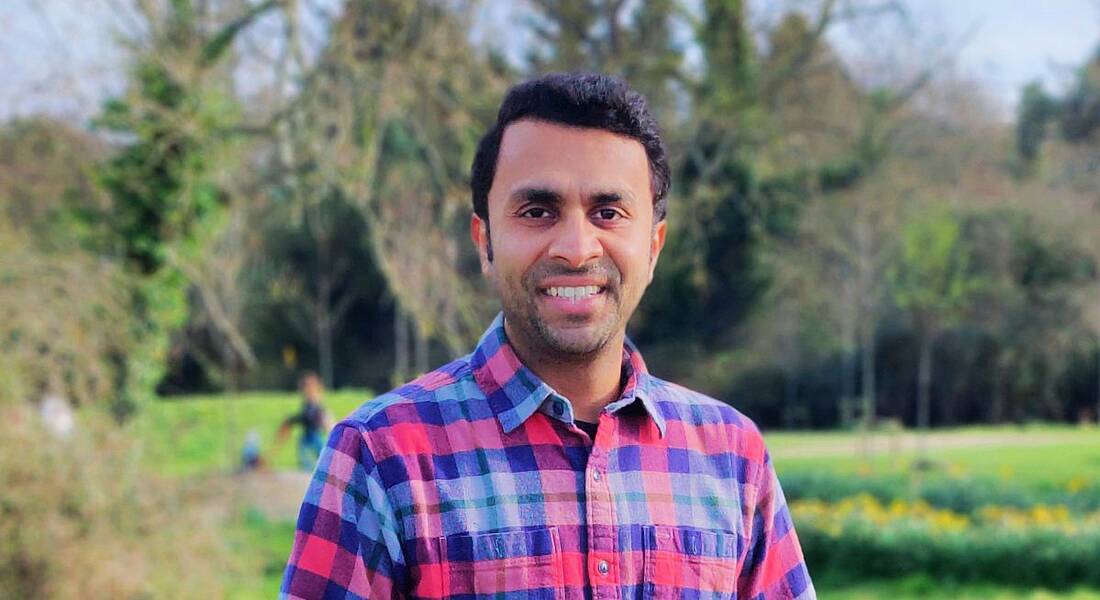 A man stands smiling in a field with forestry behind him. He is Vivek Shah, vice-president of technology management at Fidelity Investments.