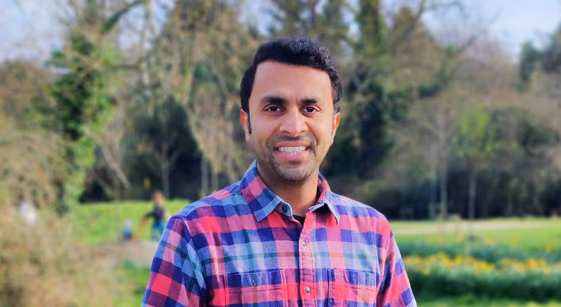 A man stands smiling in a field with forestry behind him. He is Vivek Shah, vice-president of technology management at Fidelity Investments.