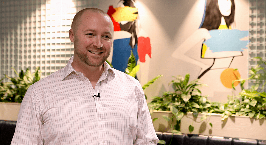 A man in a salmon pink shirt smiles in an office setting, with plants and paintings on the wall behind him. He is Daniel Hunt, head of engineering at Zalando.