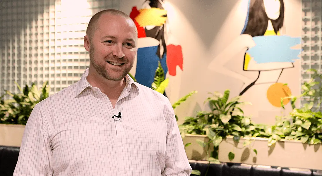 A man in a salmon pink shirt smiles in an office setting, with plants and paintings on the wall behind him. He is Daniel Hunt, head of engineering at Zalando.