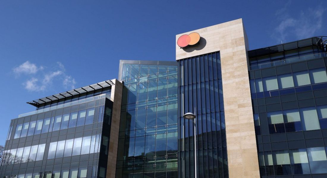 A large glass building with the Mastercard logo on the side against a blue sky.