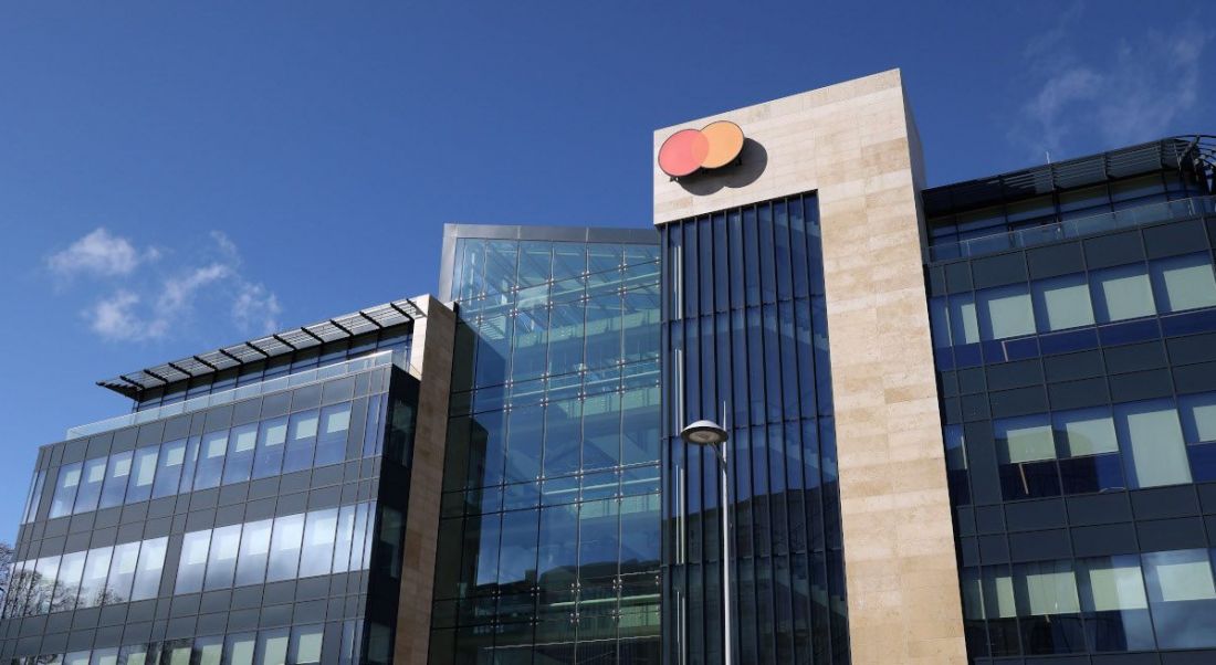 A large glass building with the Mastercard logo on the side against a blue sky.