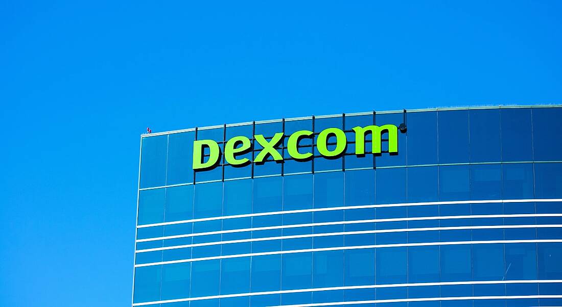 The Dexcom logo on the top of a building, with a clear blue sky behind it.