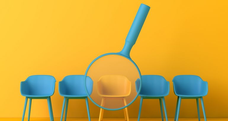 A yellow chair in the centre of a row of blue chairs on a yellow background. There is a blue magnifying glass hovering over the yellow chair.