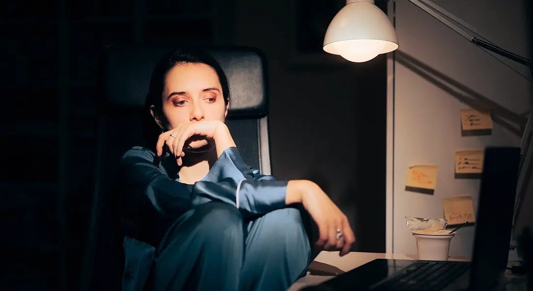 Woman sitting alone in a home office with a lonely expression on her face.