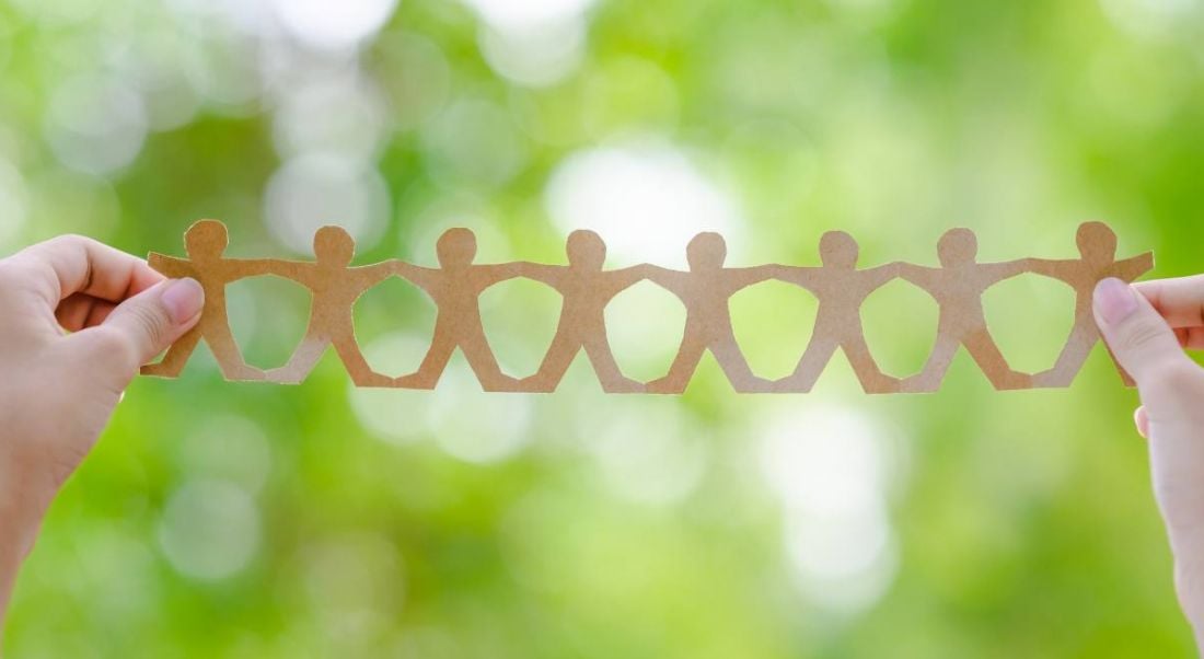 Hands holding a chain of brown paper men against a green nature-style background, symbolising CSR initiatives.