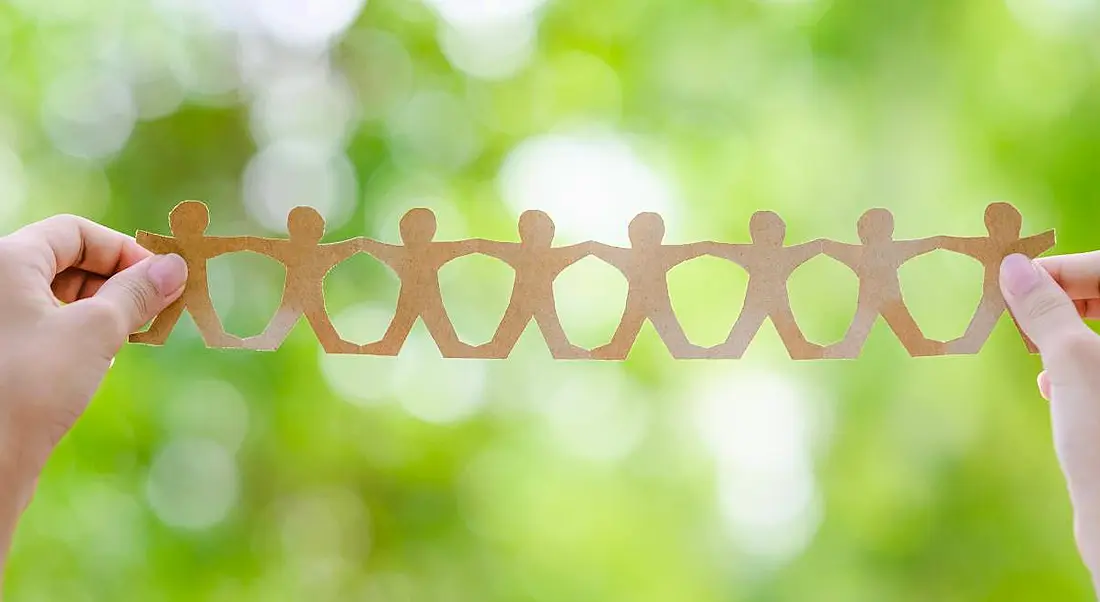 Hands holding a chain of brown paper men against a green nature-style background, symbolising CSR initiatives.