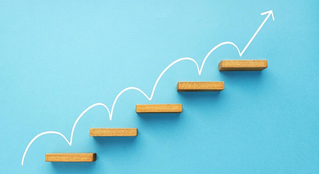 A white arrow bouncing upwards on wooden shelves against a blue background, symbolising career progression.