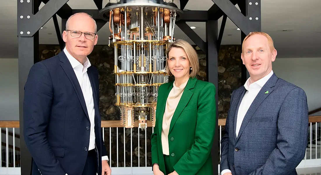 Three people standing in front of an abstract sculpture made to look like a robotics structure.