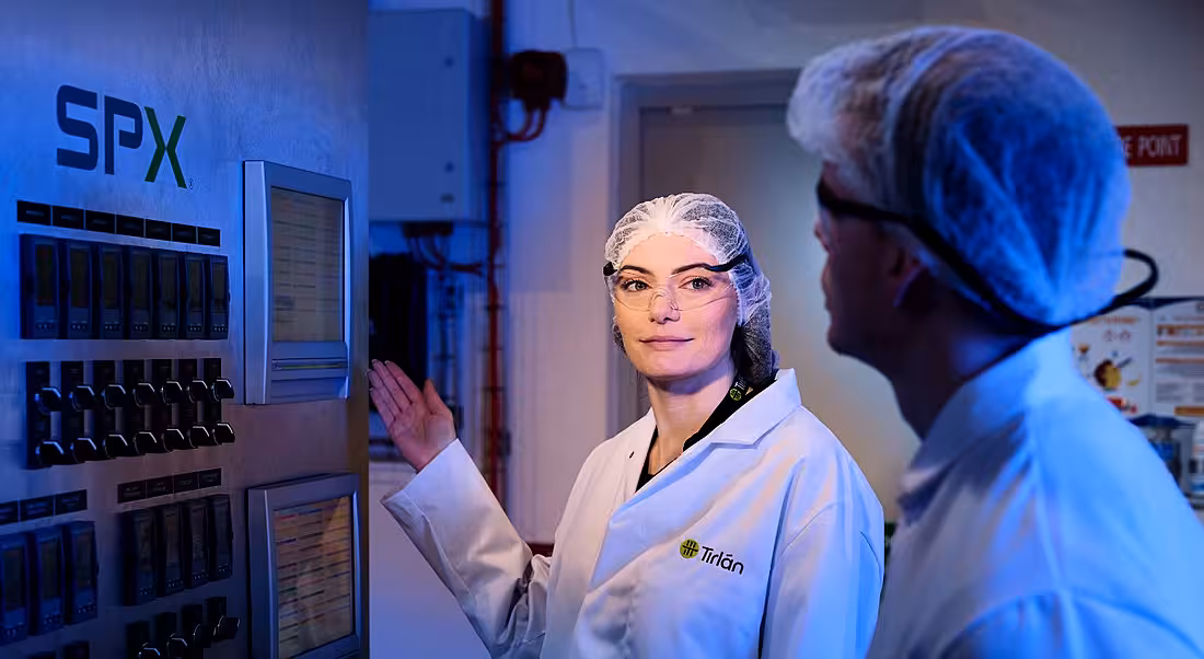 Two people who work with Tirlan wearing lab gear and standing in front of a machine.
