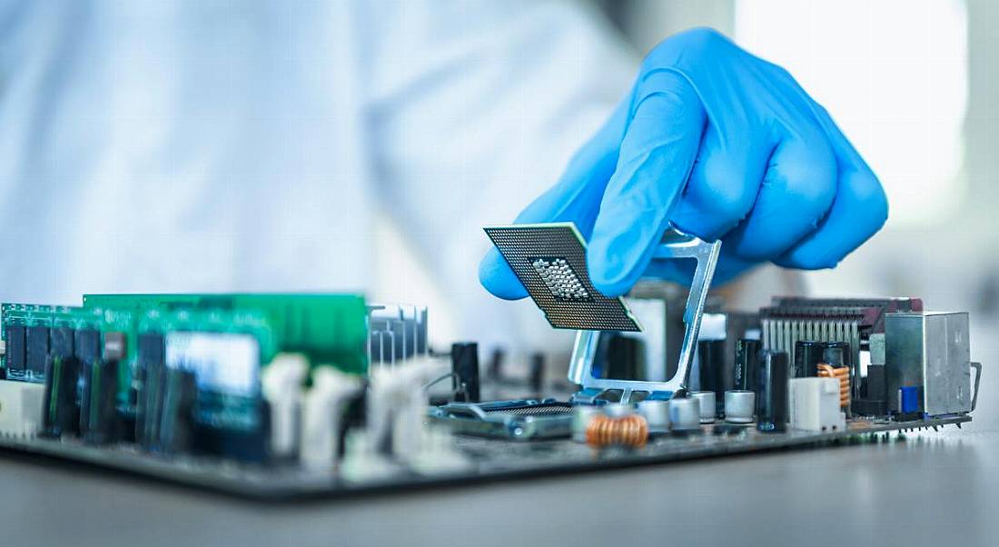 An engineer wearing blue gloves holding a chip over the inside of a computer, symbolising the chips industry.