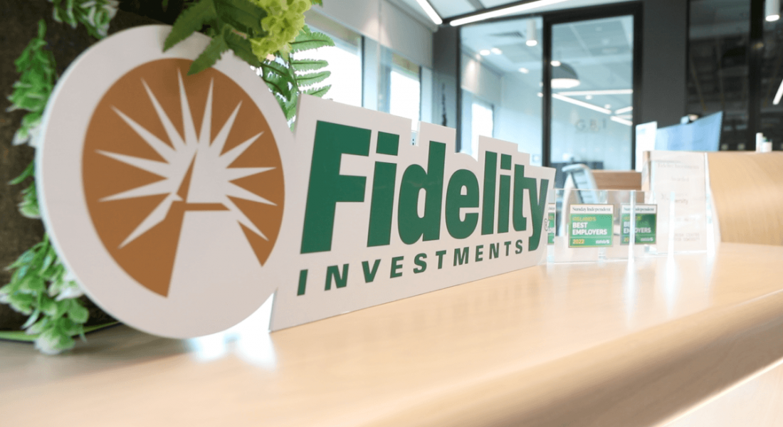 A sign depicting the logo of Fidelity Investments sits on a desk in an office setting.