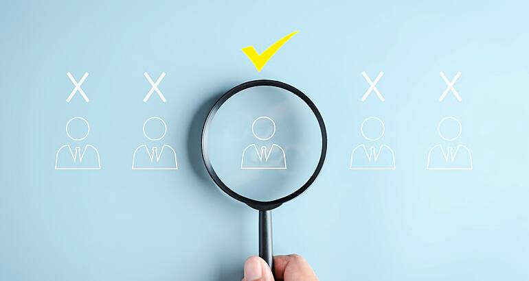 A magnifying glass held over an outline of a person with a tick mark on top. There are other candidates either side.