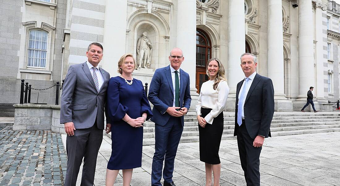 Three men and two women standing together with a large building with steps and columns behind them.