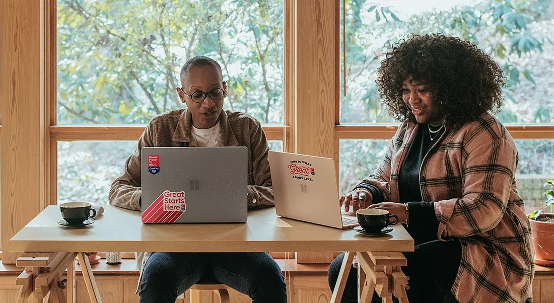 Two people on laptops at a table smiling as they work.