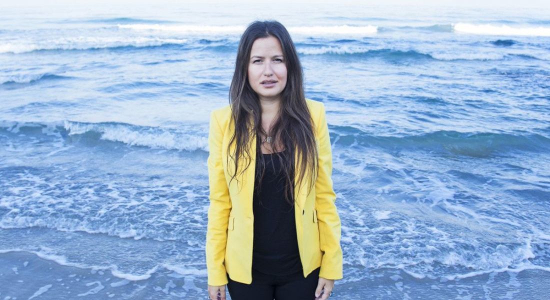 Inna Braverman of Eco Wave Power standing in front of the sea shore with waves visible behind her.