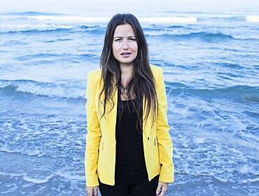 Inna Braverman of Eco Wave Power standing in front of the sea shore with waves visible behind her.