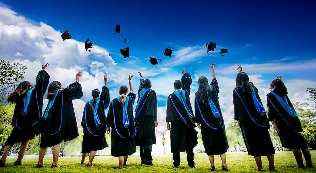 Group of graduates with their backs to the camera dressed in gowns and throwing their caps into the air in celebration.