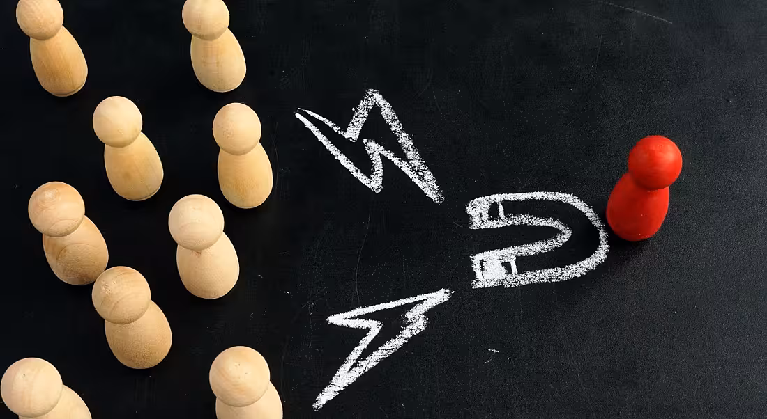 Talent attraction concept with wooden figurines facing one red figurine and chalk markings showing a drawing of a magnet and lightning symbols.