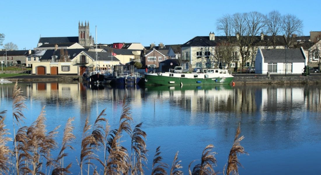 A view of Carrick-on-Shannon in County Leitrim with houses by the river bank and reeds visible.