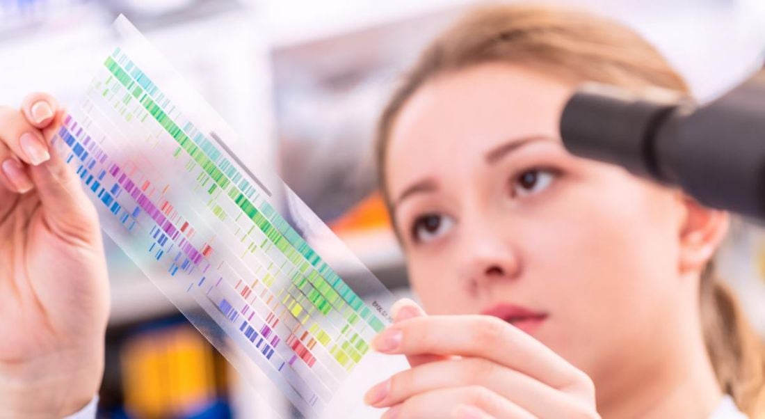 Woman in a quantum physics lab holding a sheet of transparent plastic with markings on it called a spectroscopy picture to the light so she can examine it.