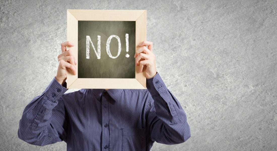 Person in a purple shirt at work holding up a chalkboard sign with the word 'no!' written on it.