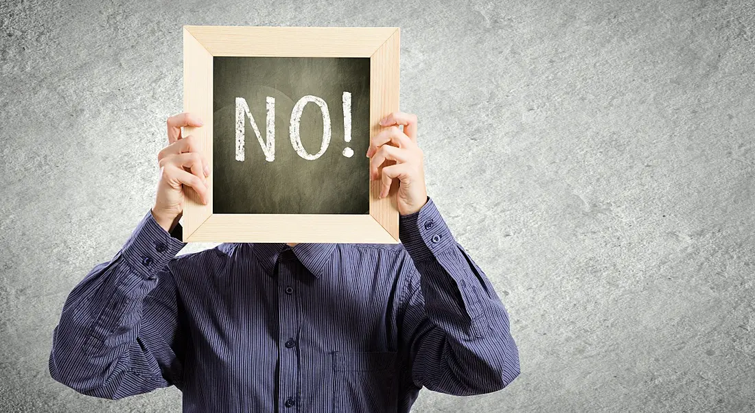 Person in a purple shirt at work holding up a chalkboard sign with the word 'no!' written on it.