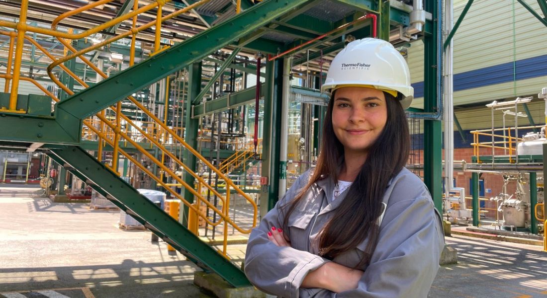 A woman wearing a hard hat smiles at the camera in an industrial site. She is Sarah Kelly, an engineer at Thermo Fisher Scientific.