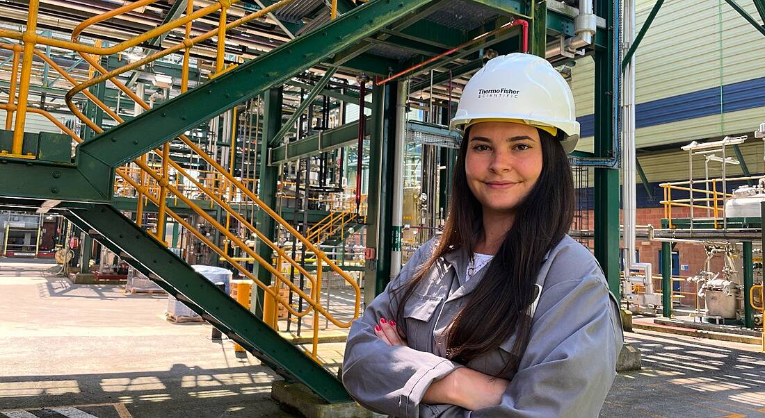 A woman wearing a hard hat smiles at the camera in an industrial site. She is Sarah Kelly, an engineer at Thermo Fisher Scientific.