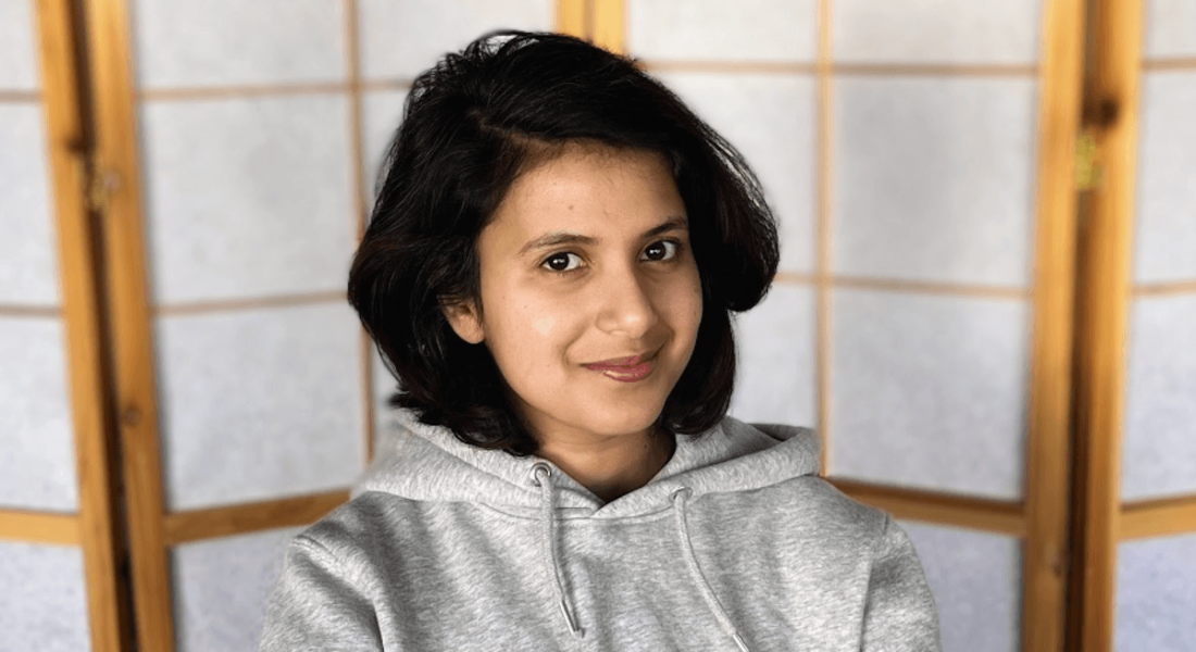 A woman wearing a grey hoodie smiles at the camera. She is Varuna C Dev, a back-end engineer at Personio.
