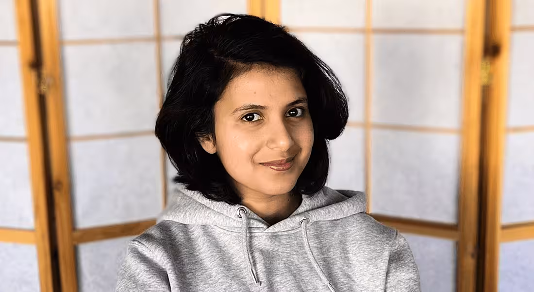 A woman wearing a grey hoodie smiles at the camera. She is Varuna C Dev, a back-end engineer at Personio.
