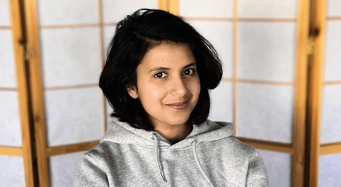 A woman wearing a grey hoodie smiles at the camera. She is Varuna C Dev, a back-end engineer at Personio.