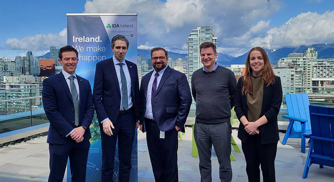 Four men and one woman stand outdoors in front of an IDA Ireland banner smiling at the camera.