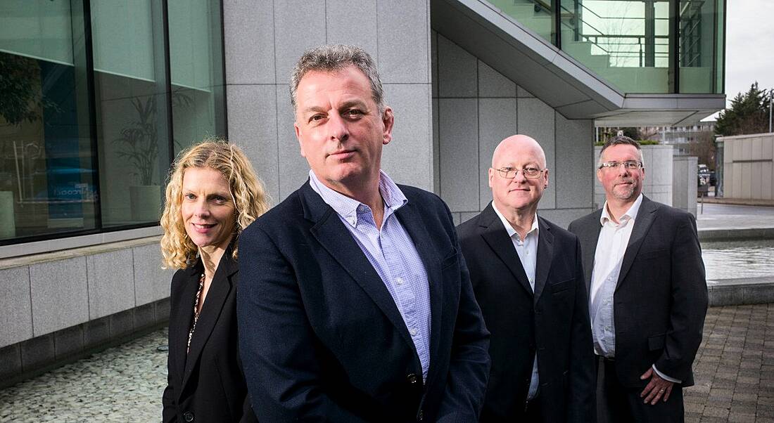 A woman and three men stand next to each other wearing business formals. They are standing in front of the Sage HQ building.