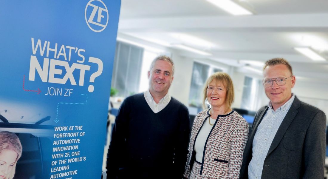 Two men and a woman stand next to each other with a poster on the left that has the ZF logo and reads "What's next?".